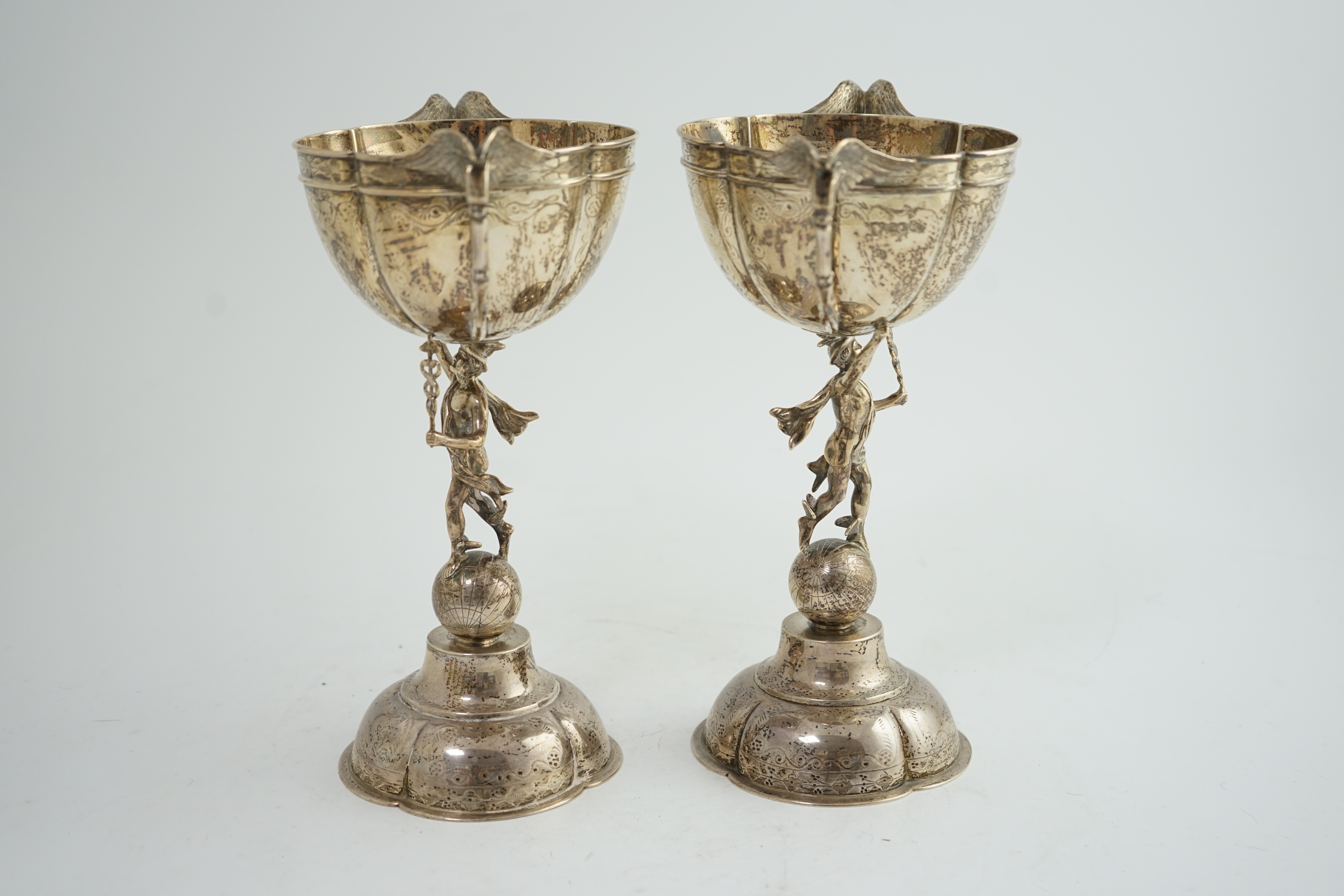 A pair of Victorian silver two handled pedestal cups, each figural stem modelled as Hermes upon a globe, by Edward Charles Brown